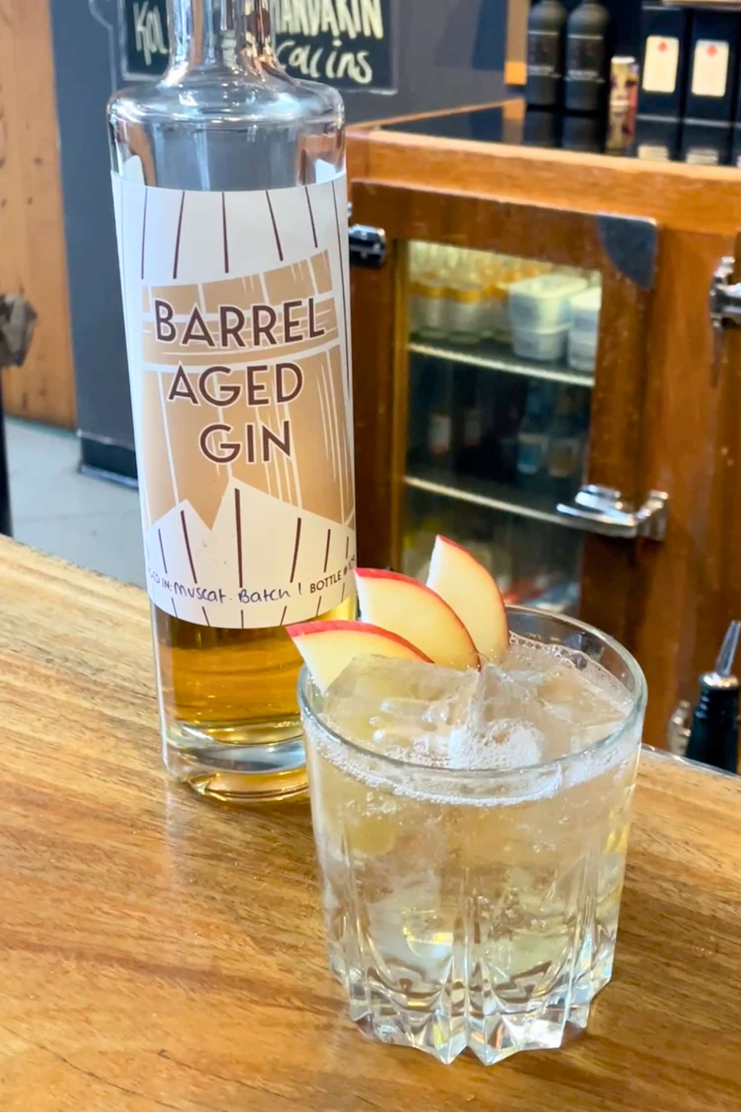 Barrel Aged Gin bottle next to cocktail in glass, garnished with fresh apple slices