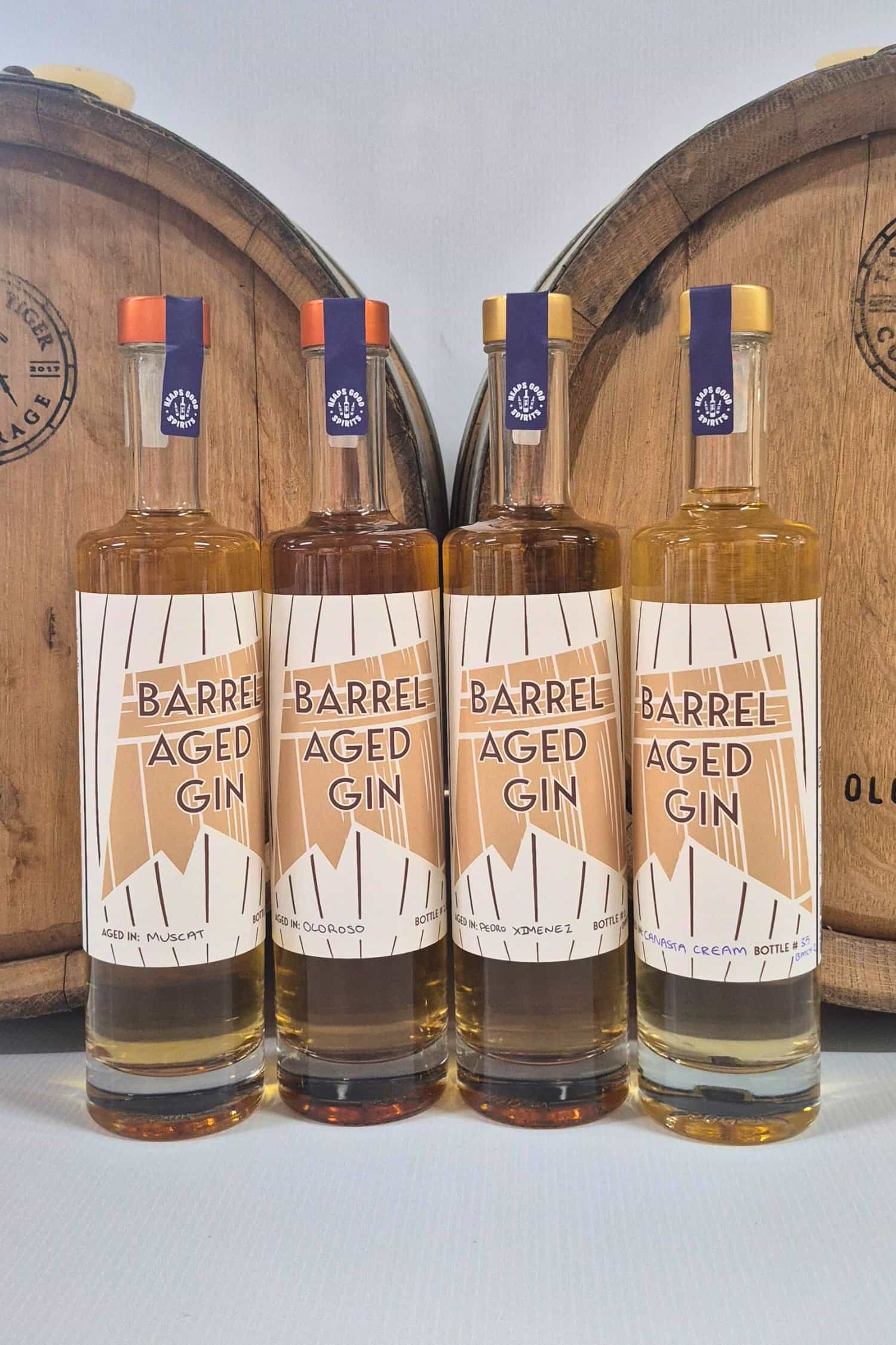 Range of four different Barrel Aged Gins by Heaps Good Spirits in front of barrels