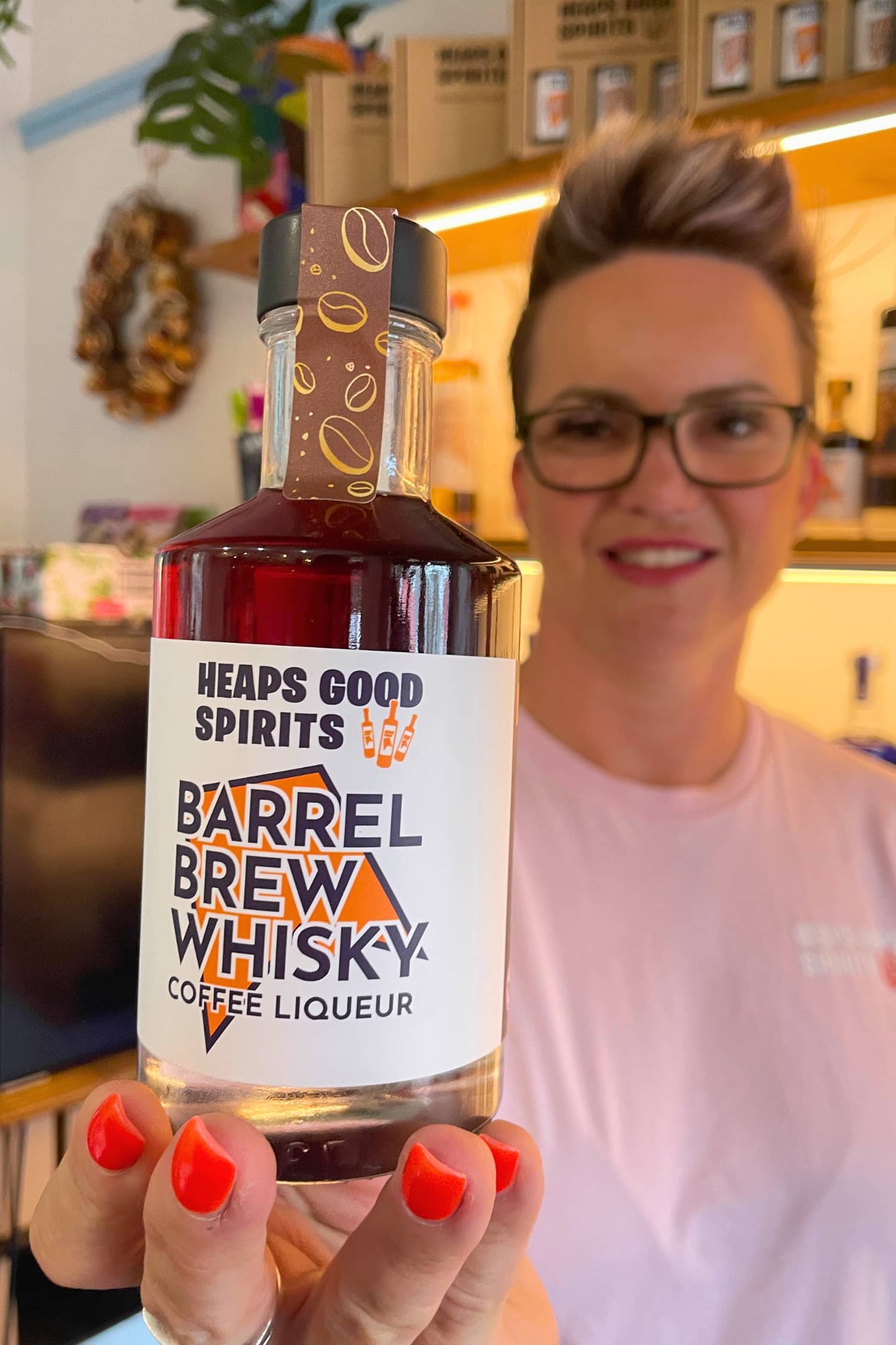 Heaps Good Spirits founder Marce holding up a 200ml bottle of Barrel Brew whisky coffee liqueur.