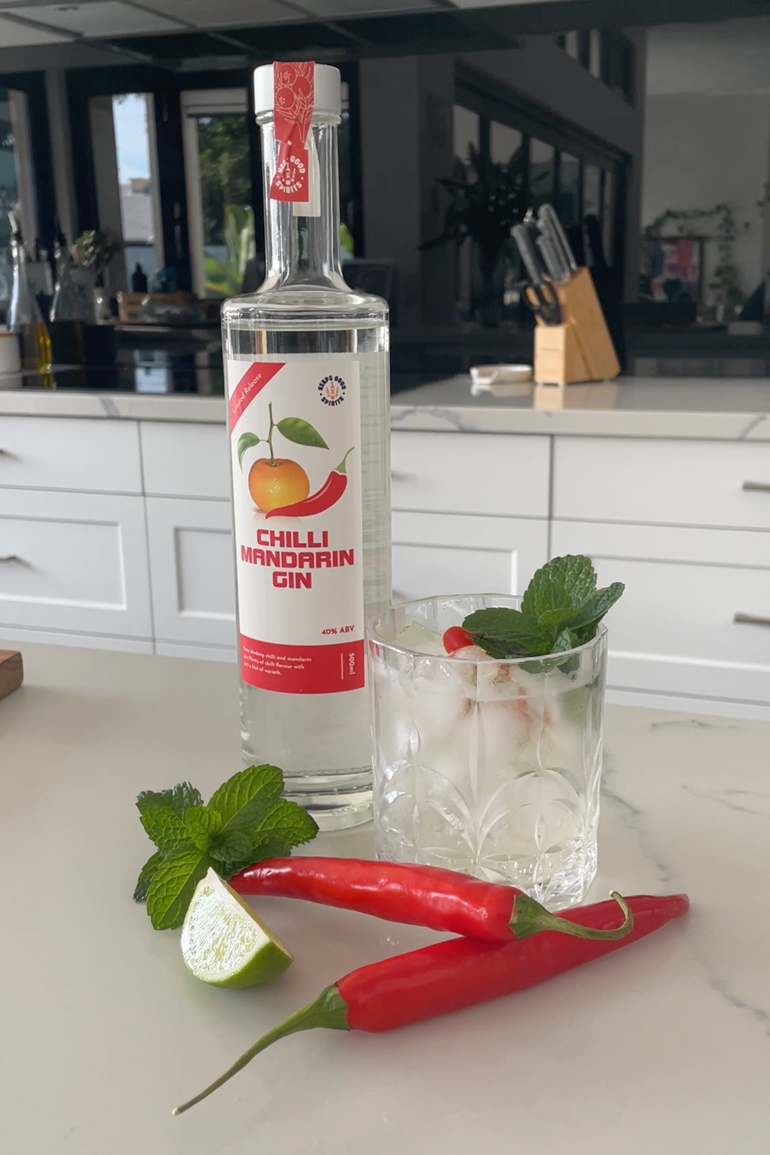 Chilli Mandarin Gin bottle with a cocktail glass, lime, and red chilli pepper on a kitchen counter.