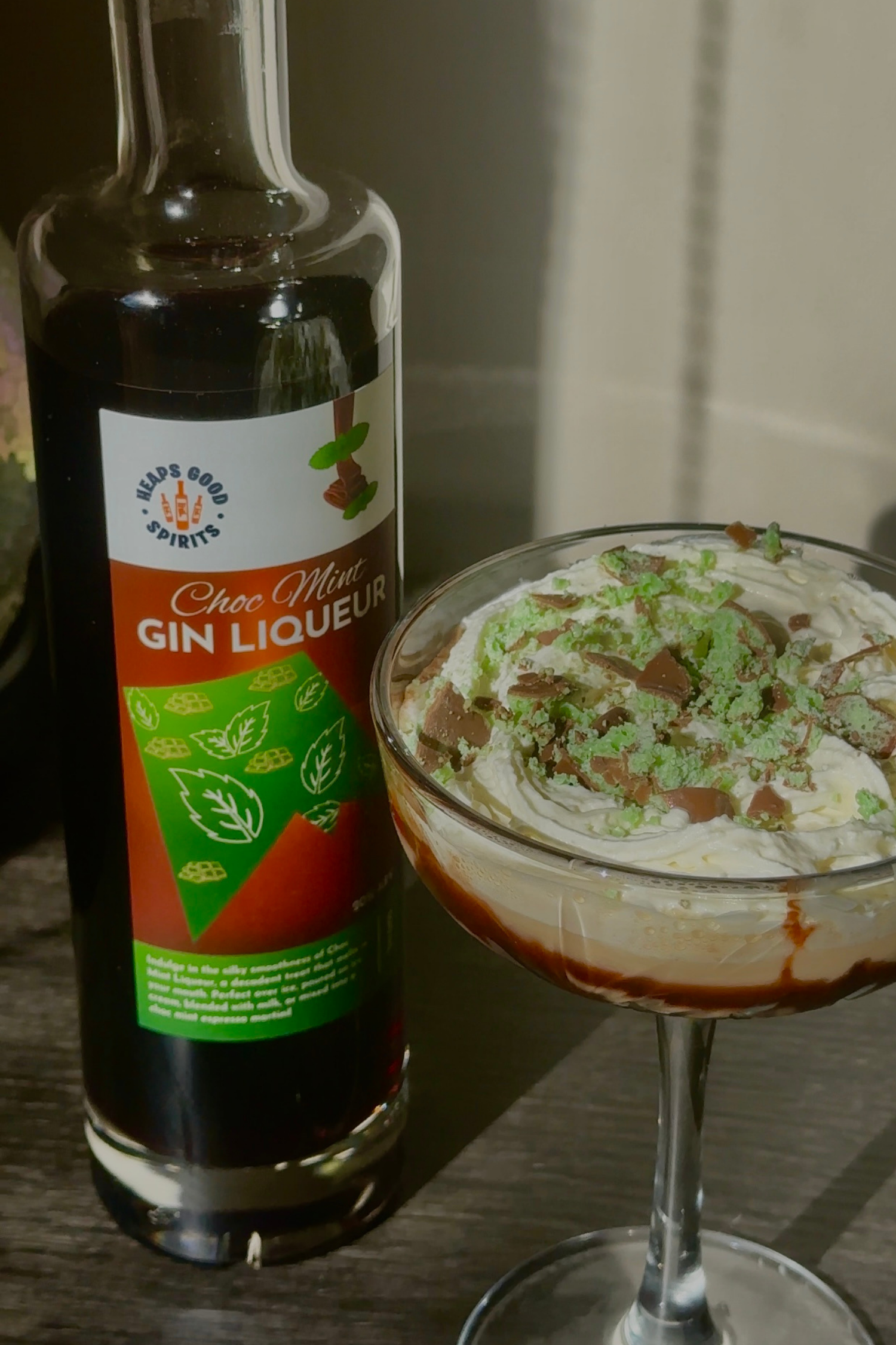Bottle of Choc Mint Gin Liqueur next to a cocktail with whipped cream and chocolate shavings.