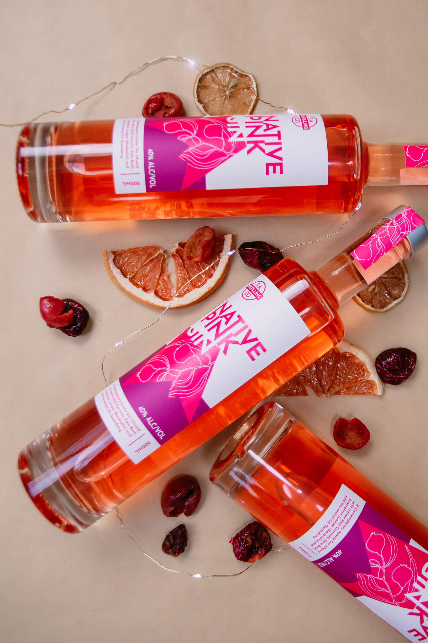Three bottles of Native Pink Gin with decorative elements on a beige background