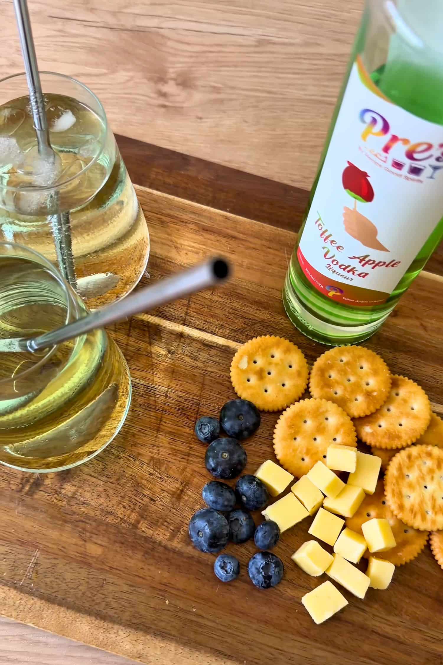 Voddi’s Toffee Apple Vodka bottle with apple soda drinks, cheese, crackers and blueberries on wooden grazing board