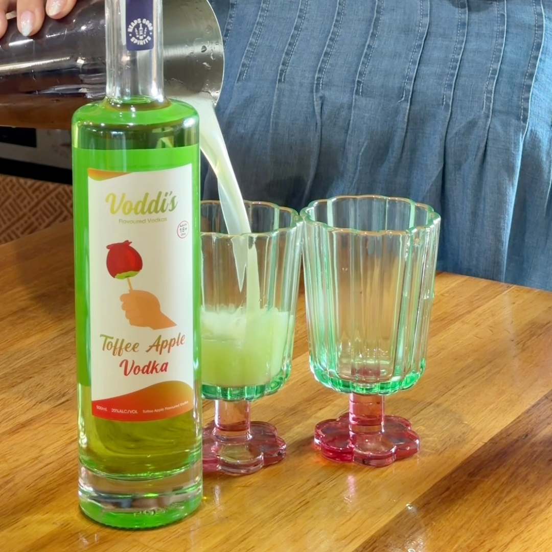 Toffee apple vodka &amp; juice cocktail being poured into a glass, beside a bottle of Voddi&