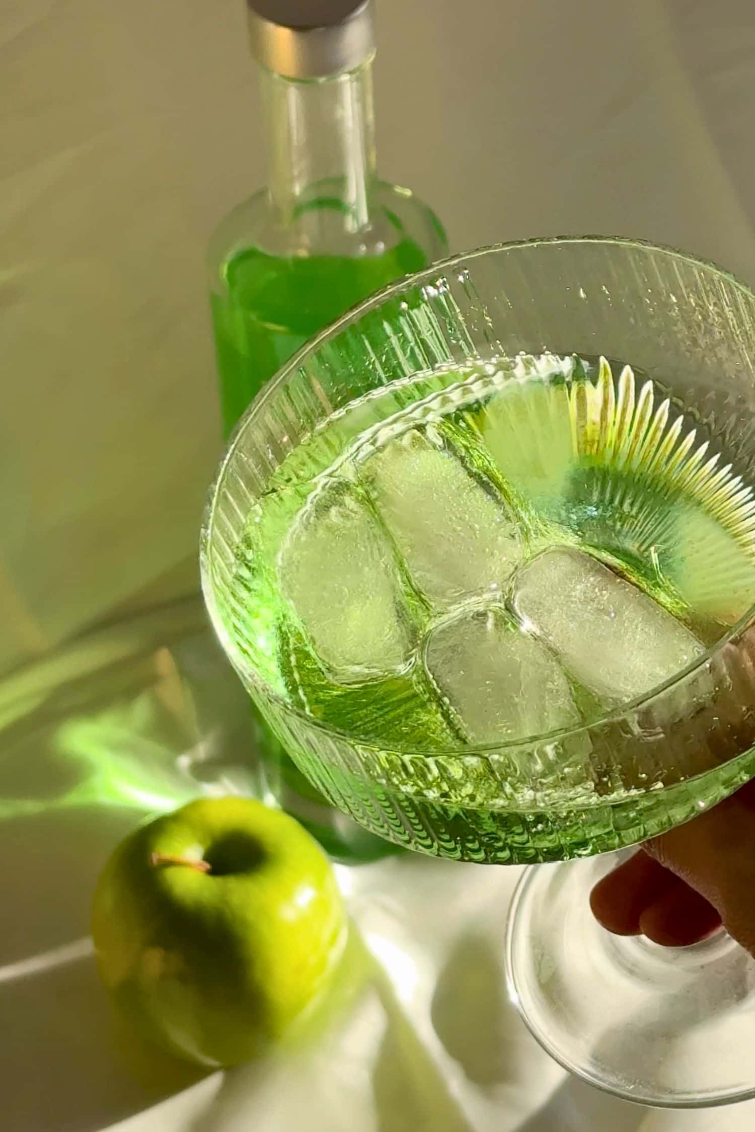 Voddi’s Green Apple Flavoured Vodka cocktail in coupe glass over ice with fresh green apple and bottle in background