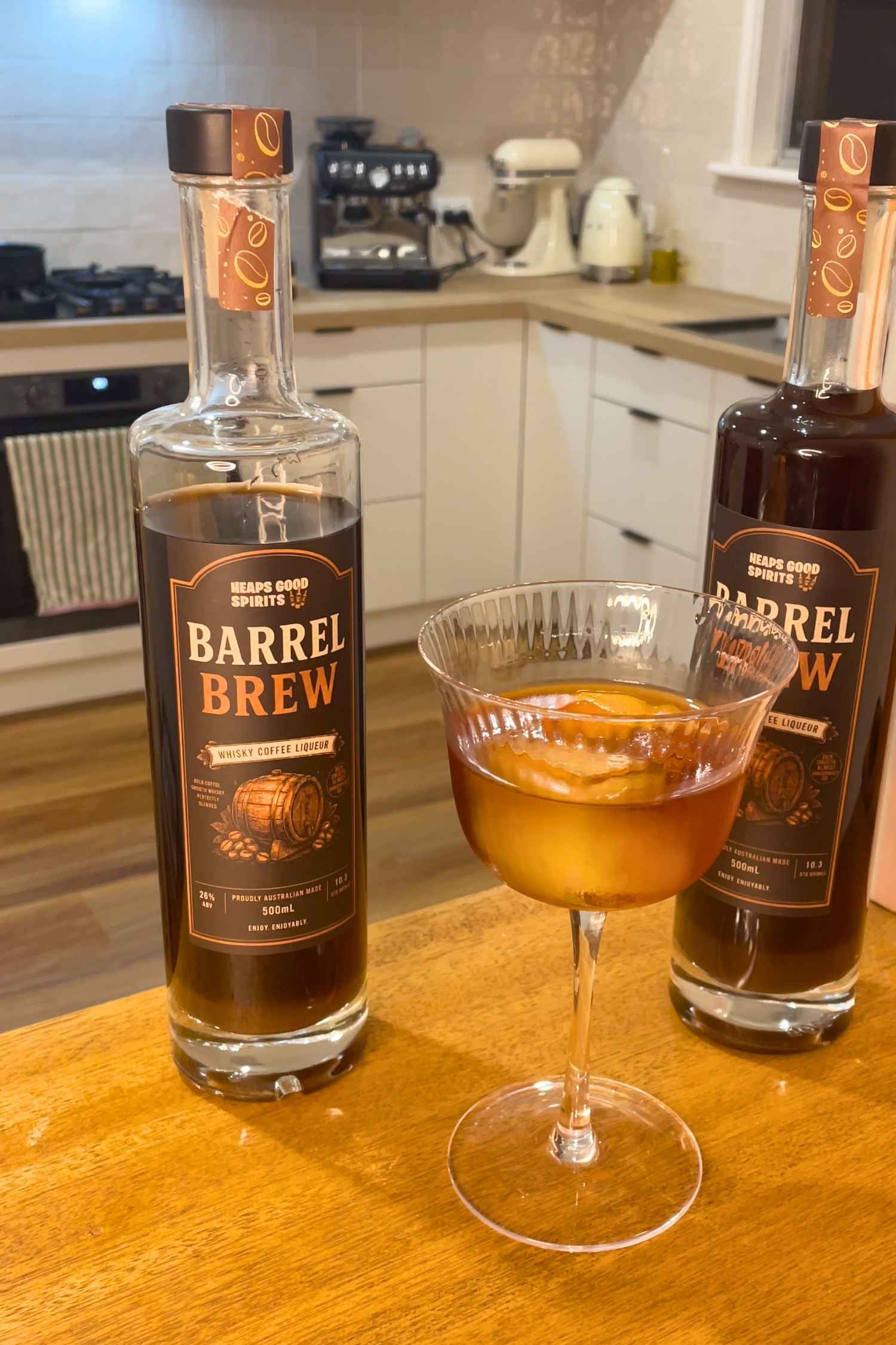 Barrel Brew whisky coffee liqueur bottle alongside a whisky coffee cocktail served in a coupe glass with an orange twist garnish.