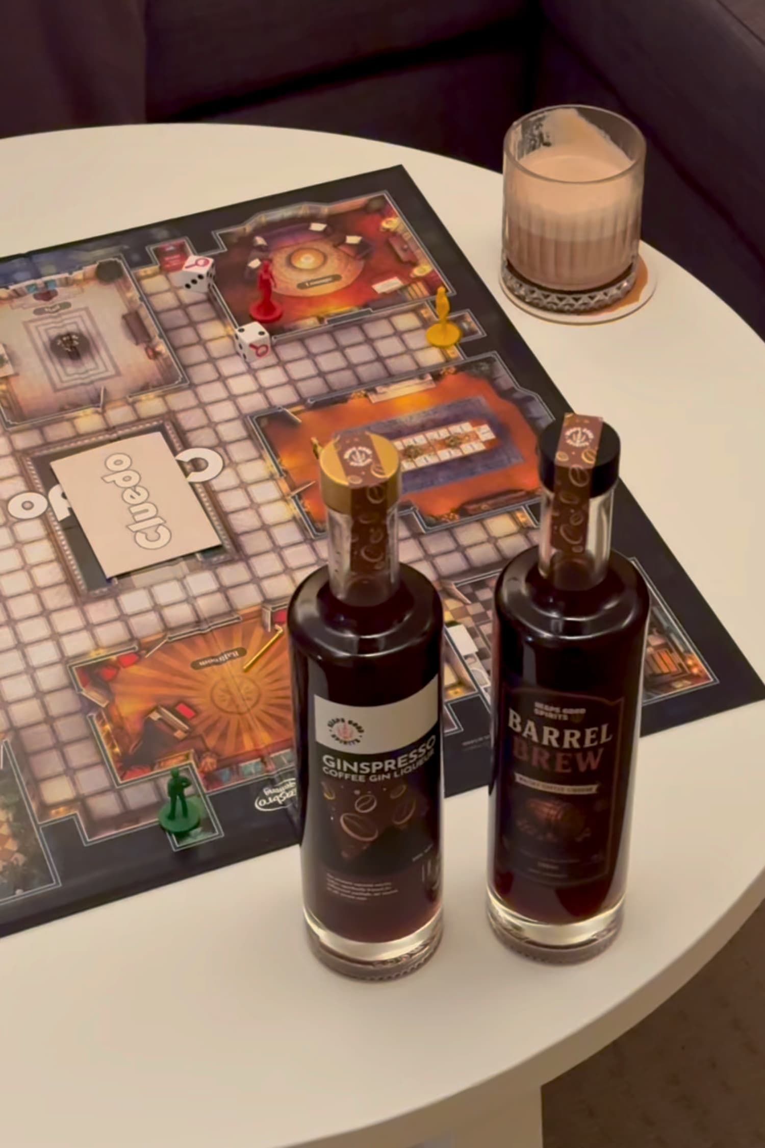 2 bottles of coffee liqueur (Barrel Brew and Ginspresso) laid out on a table for a board games night, with finished coffee whisky cocktail in a glass in the background.