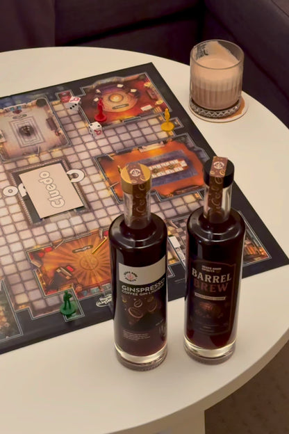2 bottles of coffee liqueur (Barrel Brew and Ginspresso) laid out on a table for a board games night, with finished coffee whisky cocktail in a glass in the background.