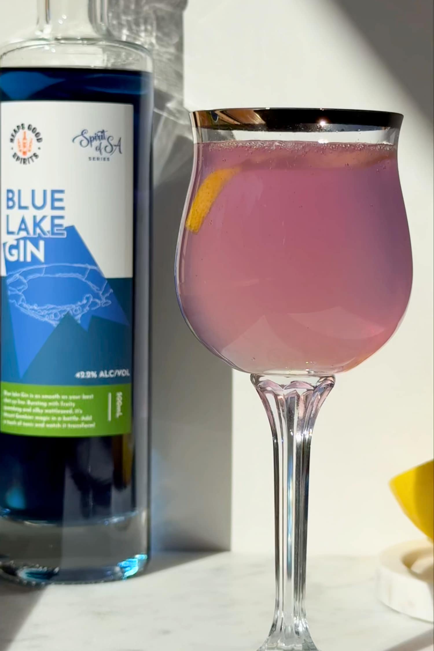 Blue Lake Gin bottle with a pink French 75 cocktail in a glass.