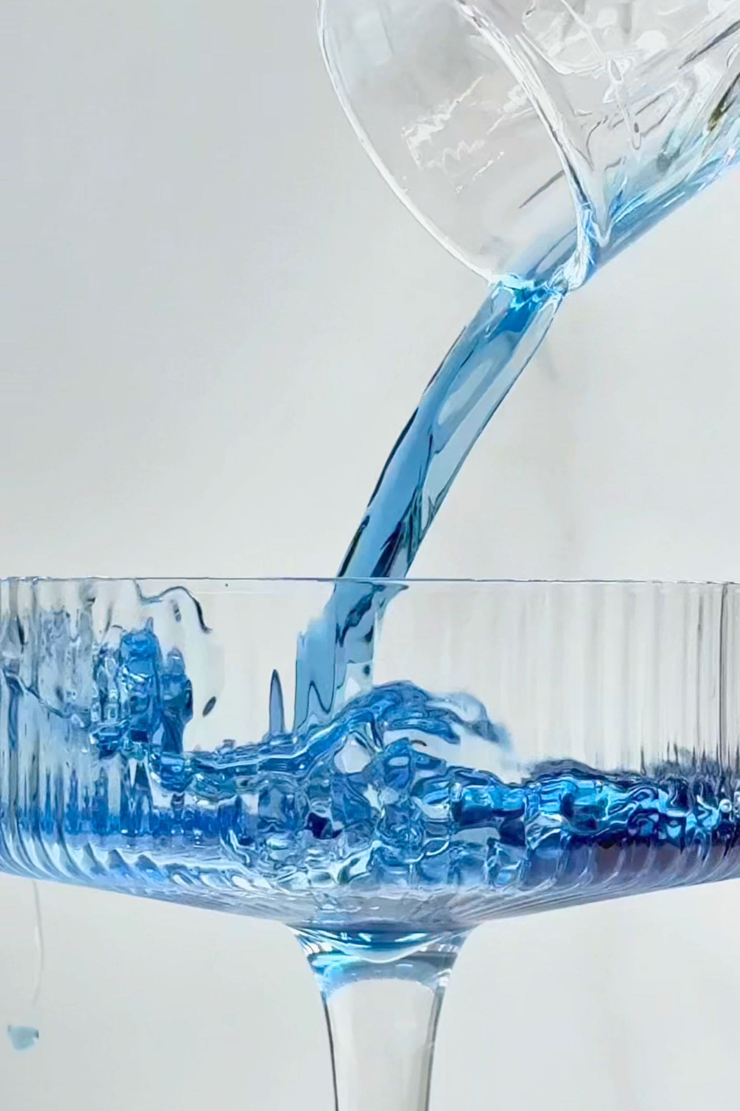 Blue Lake Gin being poured into a coupe glass, showcasing its vibrant sapphire blue gin colour before mixing.
