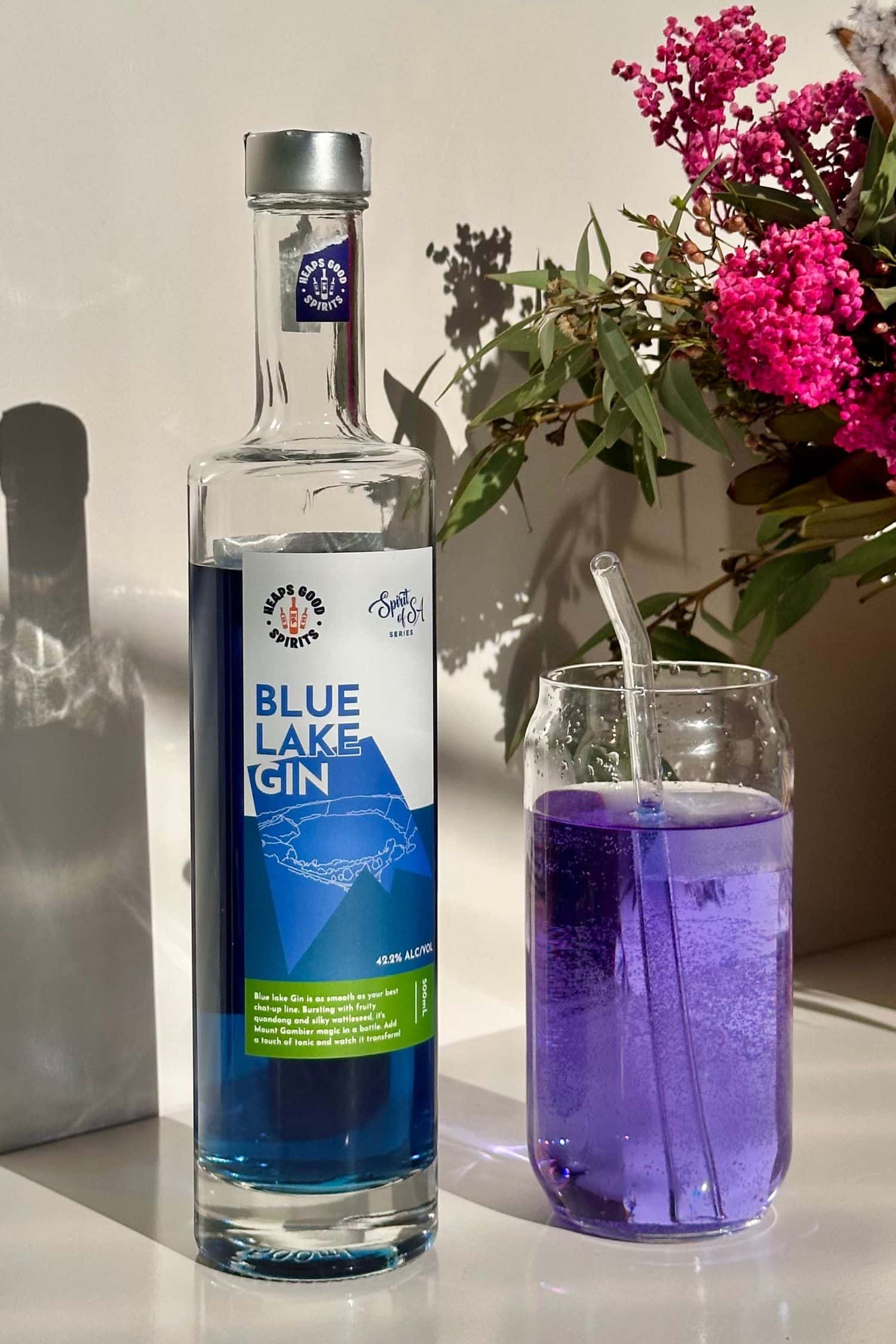 Blue Lake Gin bottle beside purple gin and tonic with flowers in background, Spirits of SA series.