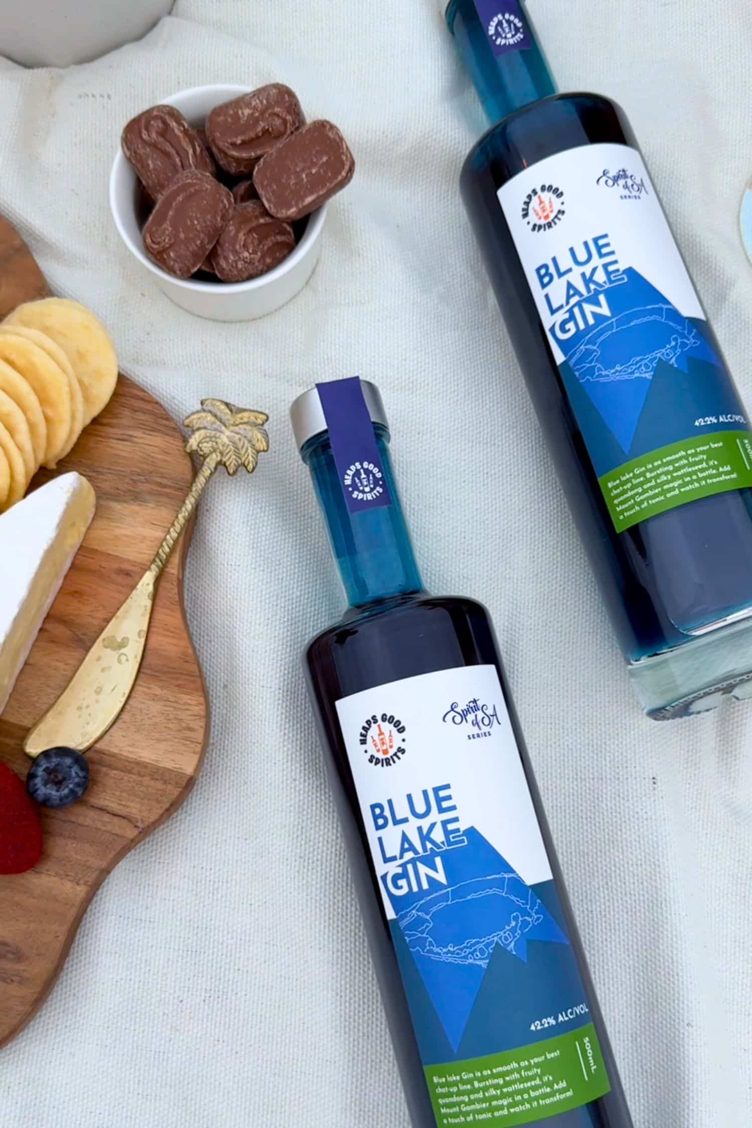 Flat lay of two Blue Lake Gin bottles with cheese board, crackers and chocolate, highlighting premium South Australian gin.