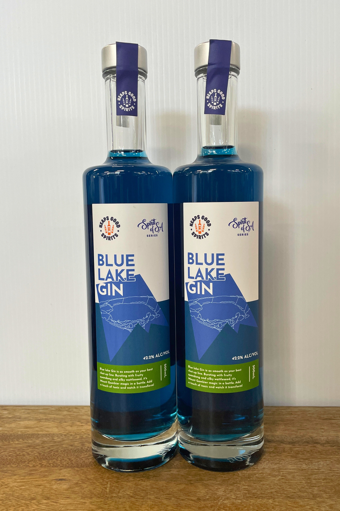 Two bottles of Blue Lake Gin on a wooden surface with a white background