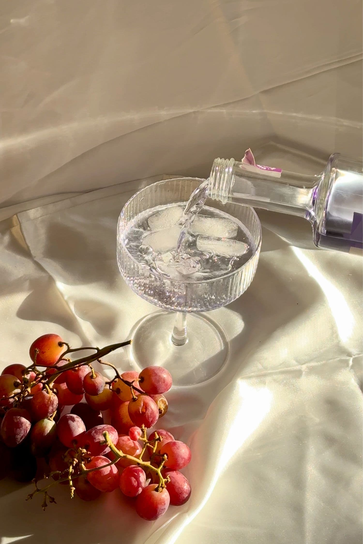 Voddi’s Bubblegum Grape Flavoured Vodka being poured into a coupe glass over ice with fresh red grapes to the side