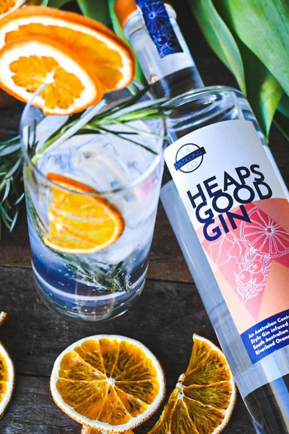 Heaps Good Gin bottle with a glass of gin and tonic garnished with orange slices on a wooden surface.