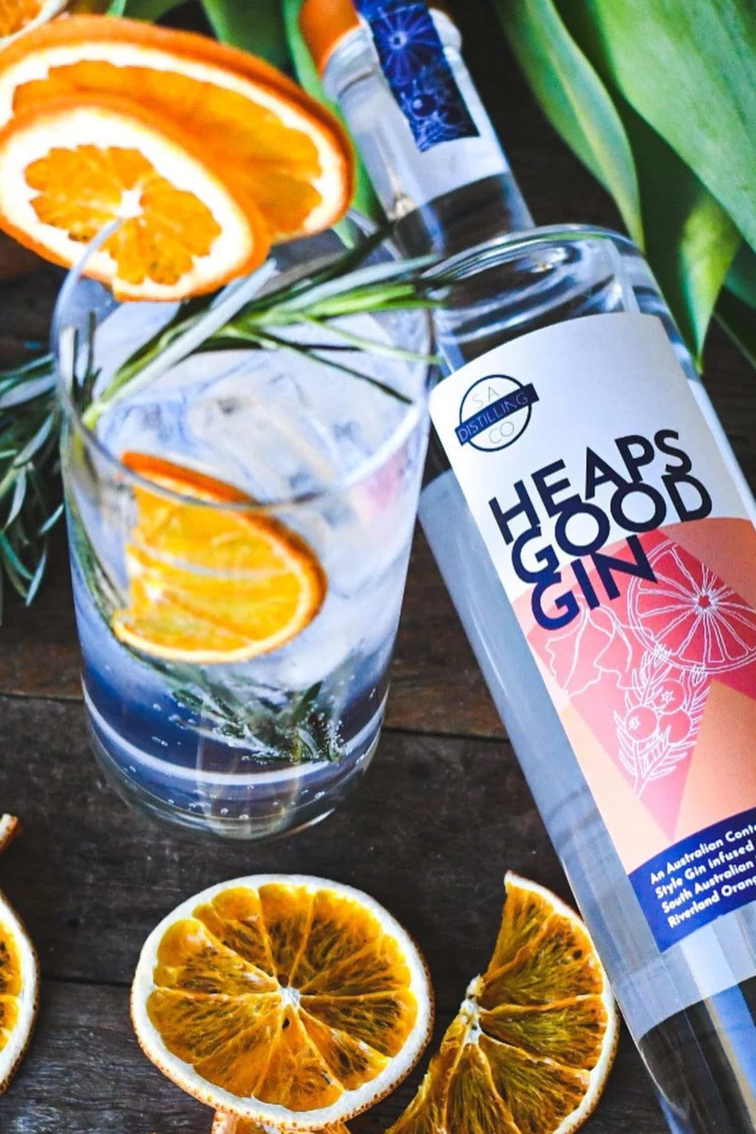 Heaps Good Gin bottle with gin and tonic garnished with orange slices and rosemary