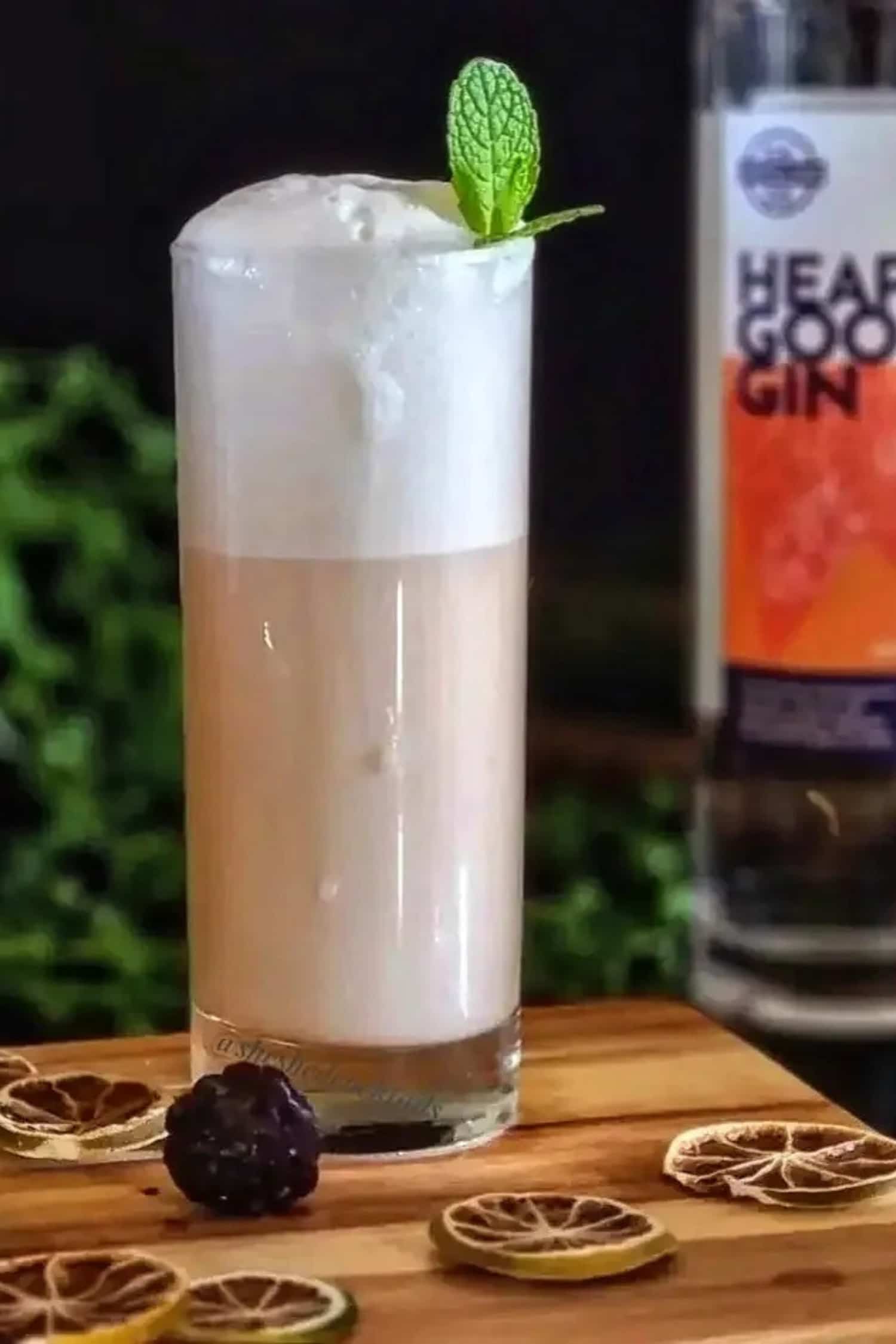 Cocktail with foam and a mint leaf, with s Heaps Good Gin bottle in the background