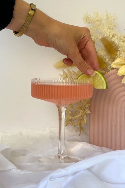 Pink gin cocktail in coupe glass garnished with fresh lime slice