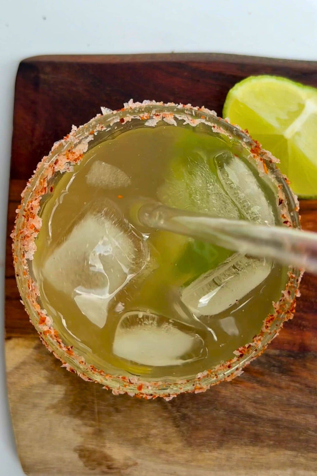 Top view of pineapple-lime margarita with chilli salt rim, fresh lime wedge and ice