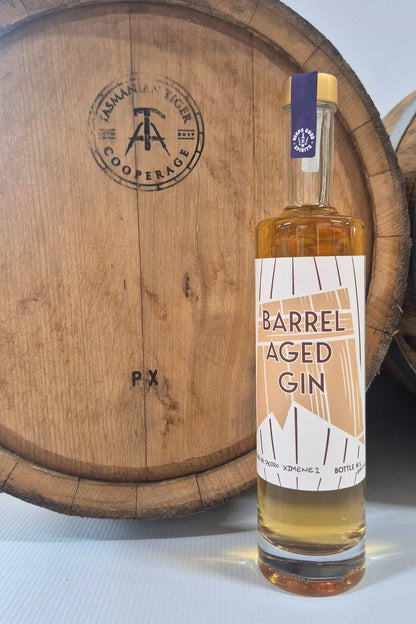 Barrel Aged Gin bottle in front of Pedro Ximenez barrel that it was aged in