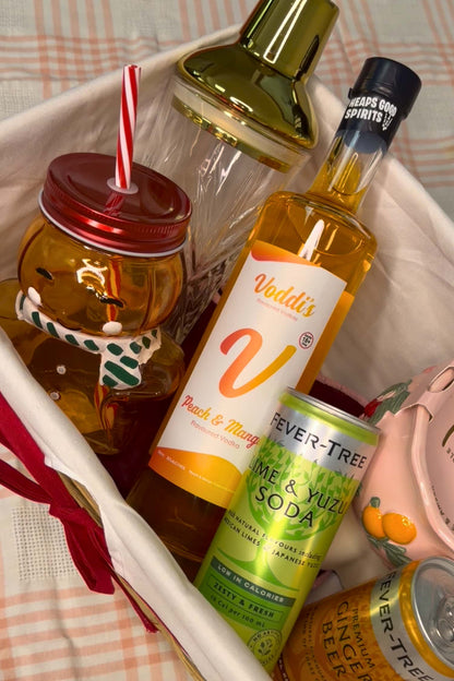 A curated gift basket containing multiple beverage-related items: a bottle of Vodd&