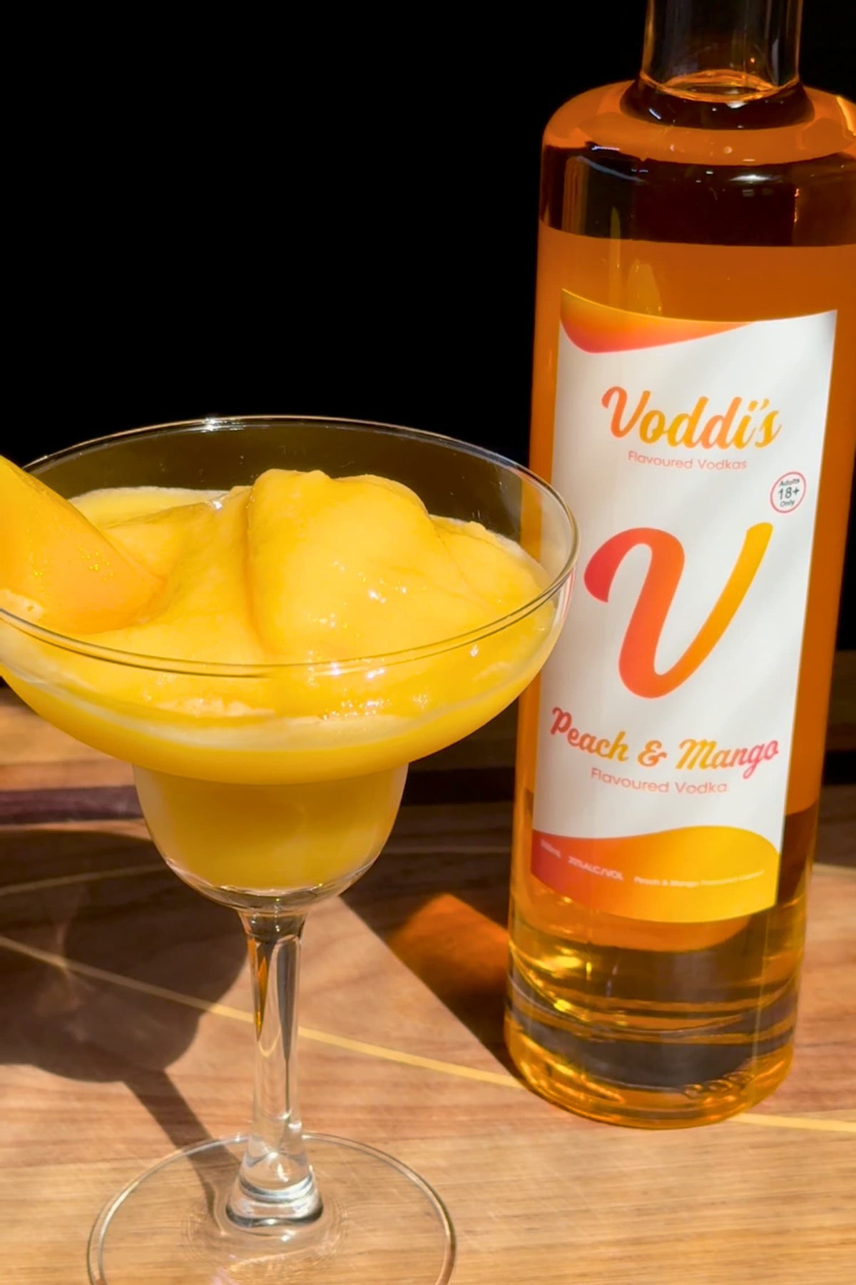 Peach &amp; Mango frozen daiquiri cocktail served next to a full bottle of Voddi&