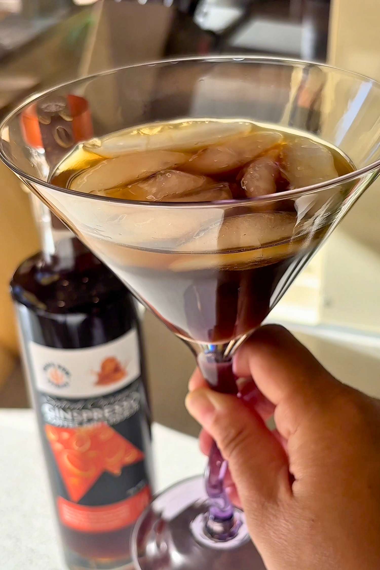 Salted Caramel Ginspresso coffee gin liqueur poured straight over ice in a glass, with a bottle in the background.