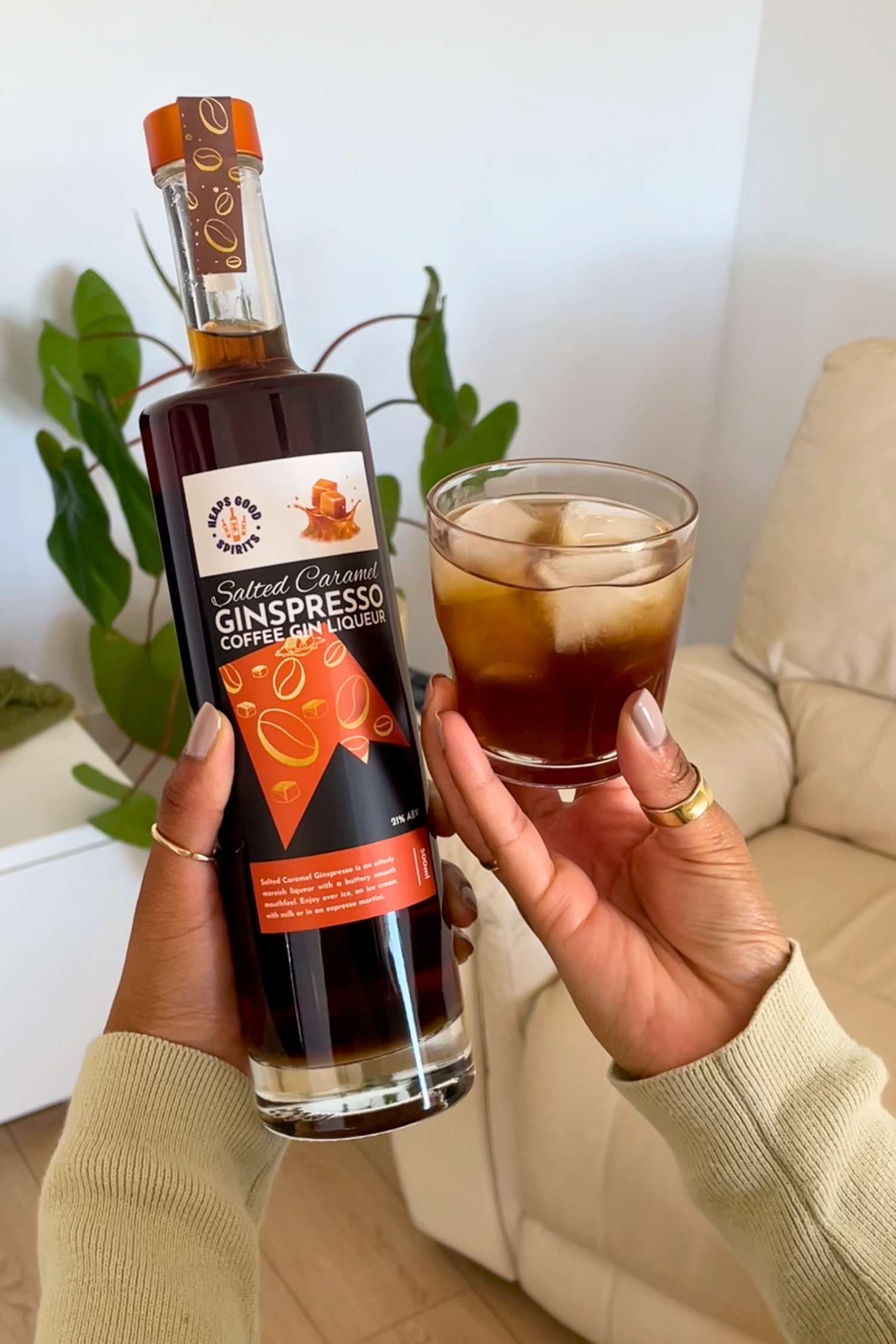 Bottle of Salted Caramel Ginspresso coffee gin liqueur held by a person with a glass of the drink poured straight over ice.
