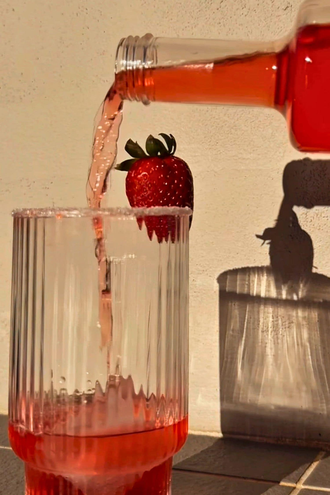 Heaps Good Strawberry Margs being poured into ribbed glass with salt rim and fresh strawberry garnish