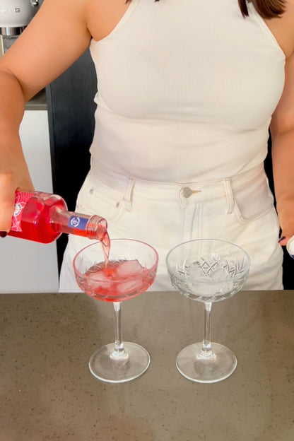 Heaps Good Strawberry Margs being poured over ice into coupe glasses on kitchen bench