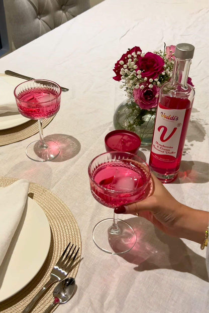 Strawberries &amp; Cream Vodka pink cocktails served in coupe glasses on a styled dinner table with roses and Voddi’s bottle.