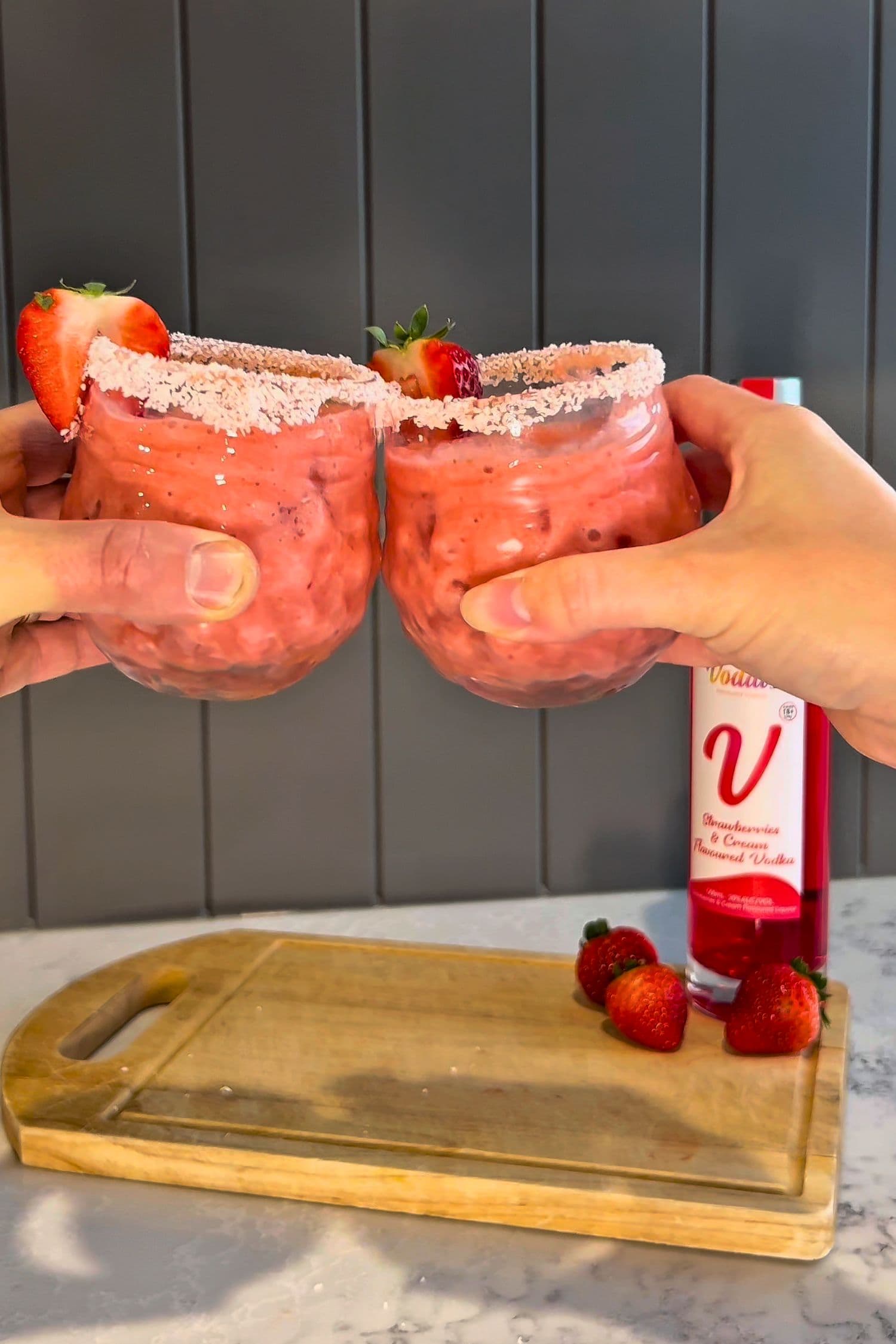 Strawberries &amp; Cream Vodka creamy strawberry cocktails with coconut rim and fresh strawberries, Voddi’s bottle in background.