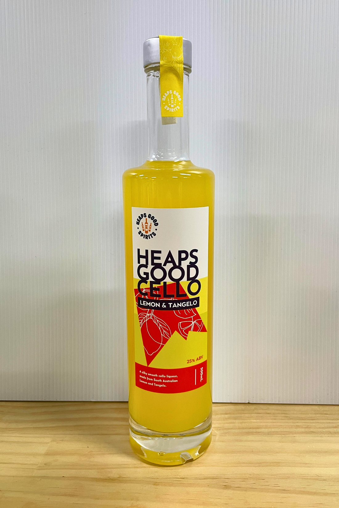 Bottle of Heaps Good Lemon &amp; Tangelo Cello on a wooden surface with a white background