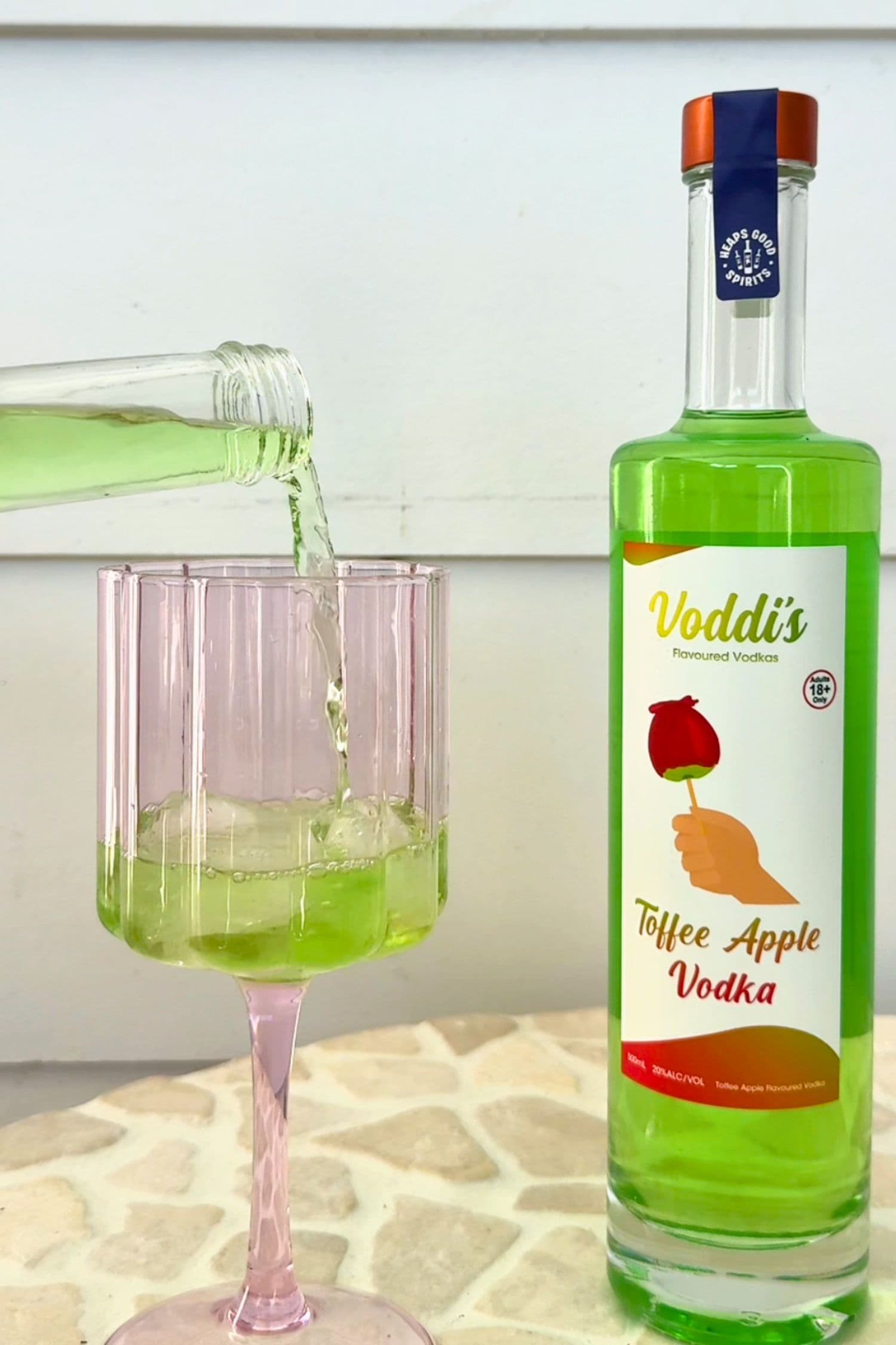 Pouring Voddi’s Toffee Apple Vodka into glass with bottle beside it.